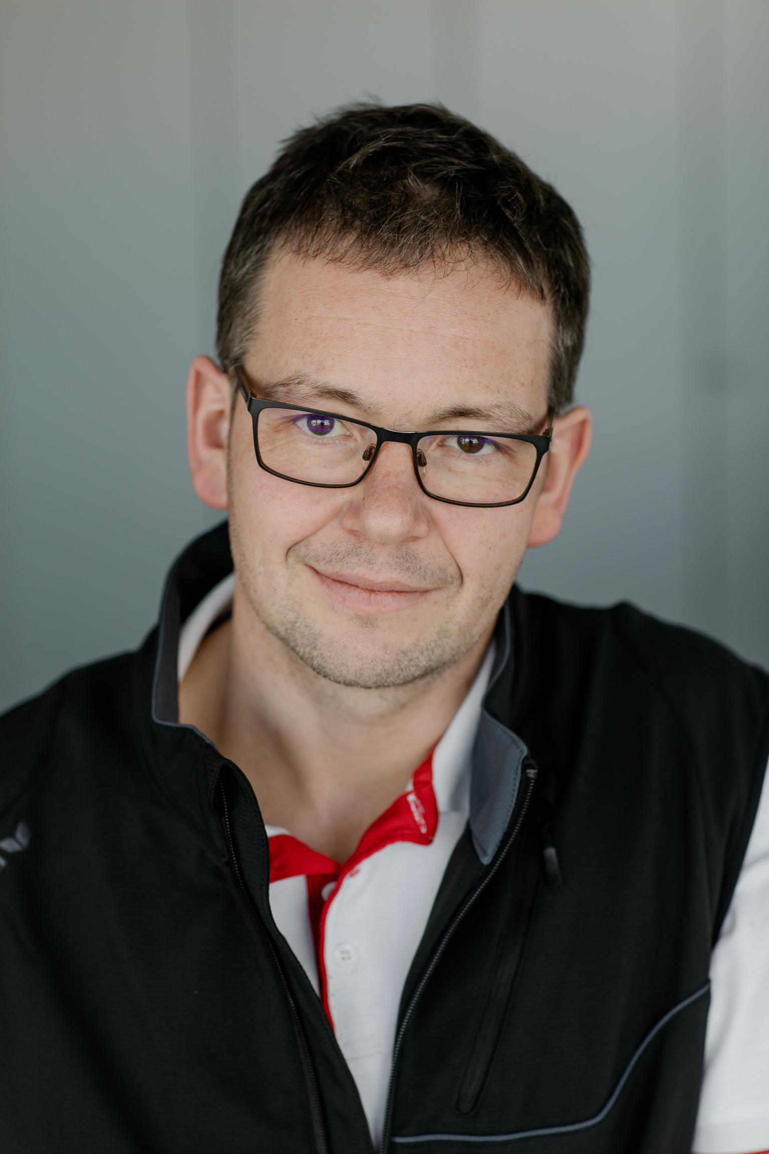 Andreas Bausch im Portrait mit dunkler Weste und weißem Polohemd mit roten mbk Akzenten.