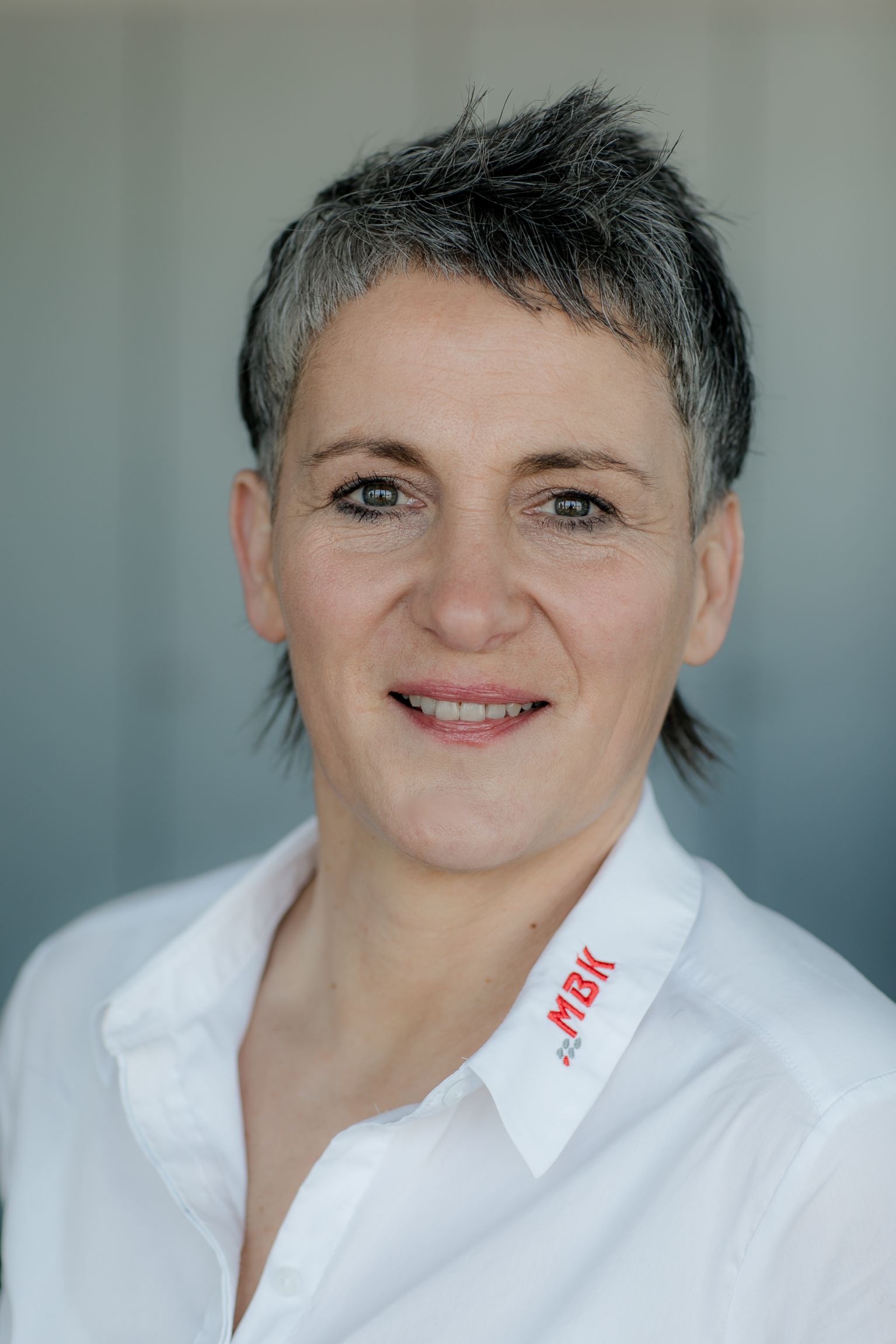 Silvia Kunz im Portrait. Sie trägt eine weiße Bluse mit mbk Logo in Rot auf dem Kragen.